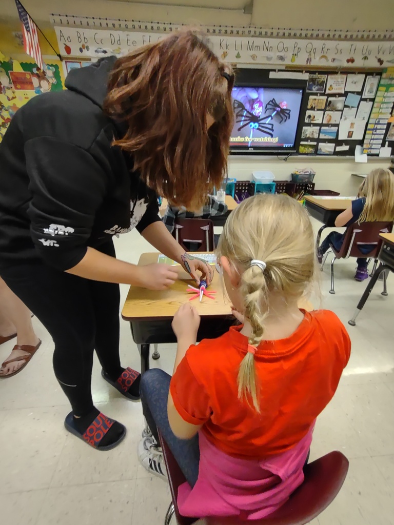 a FFA student helps a younger student at his desk make a craft with glue
