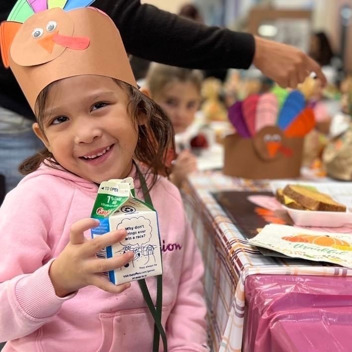 girl wearing turkey hat holding milk smiling