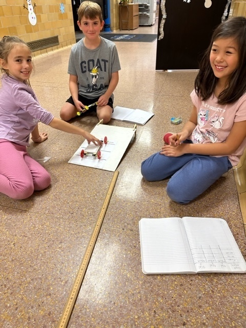 group of three students, sitting in the hallway, testing car designs