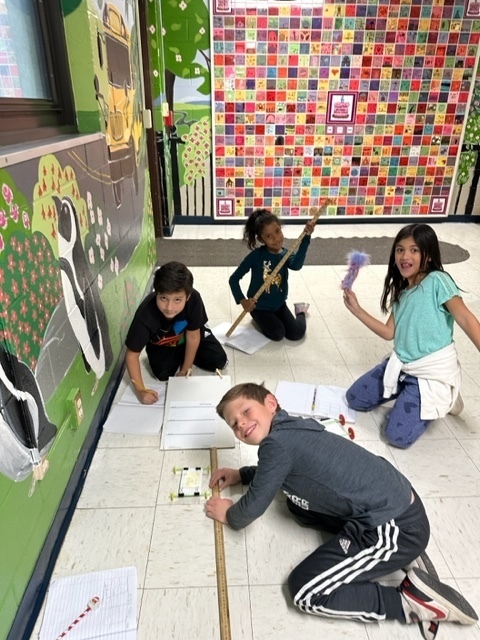 group of four students, working in the hallway, testing car designs