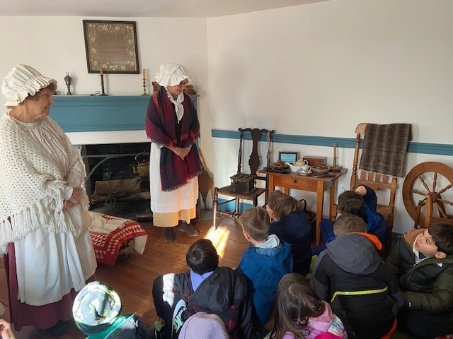 second grade class sitting in a room at the Miller Cory House museum, listening to two women speak