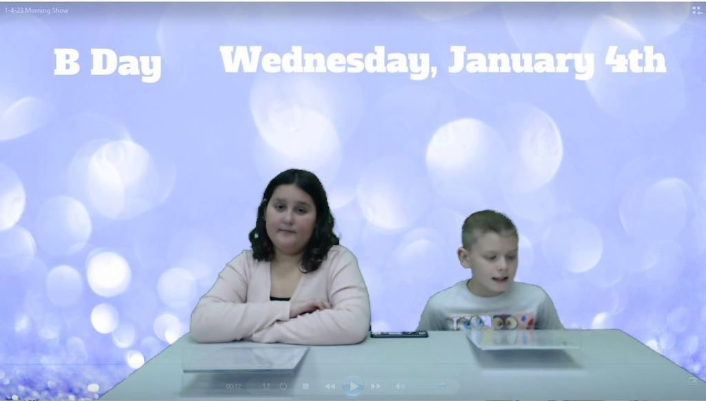 two students at news desk with a sparkly blue green screen