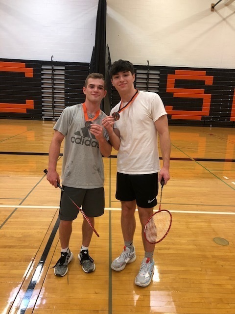 two students with badminton raquets and medals around their necks