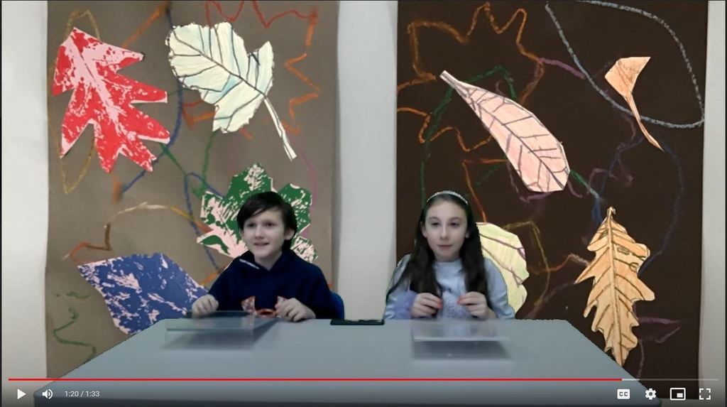 two students at news desk with art projects of leaves on the green screen