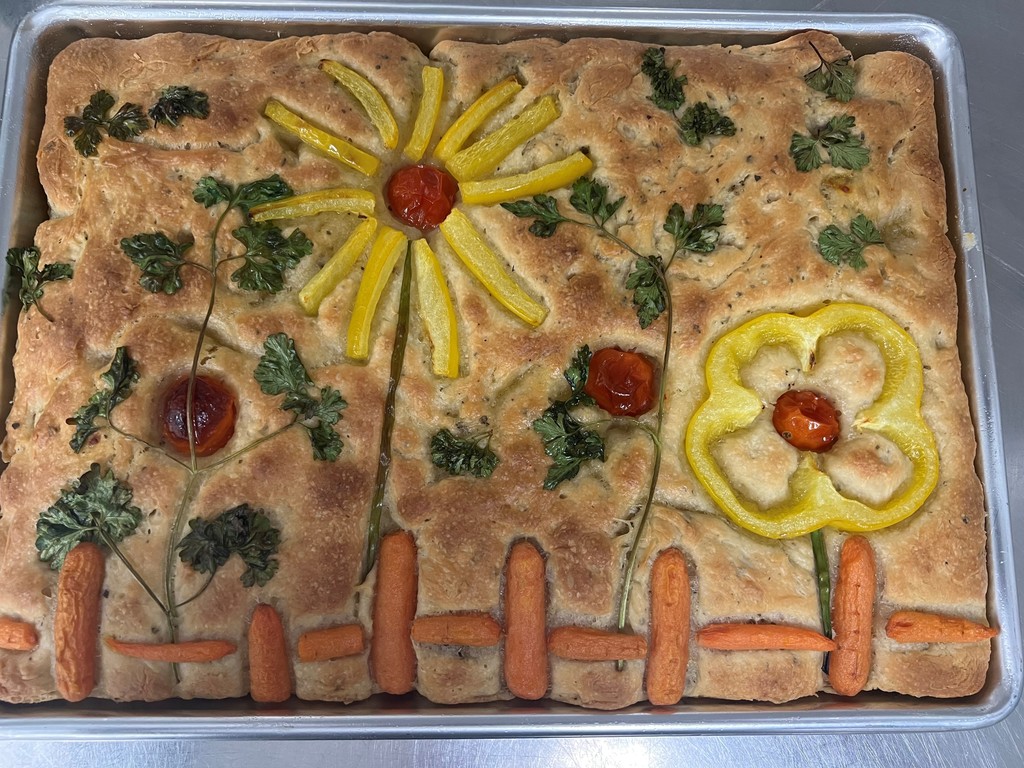 A gardenscape focaccia bread with flowers and a fence. 