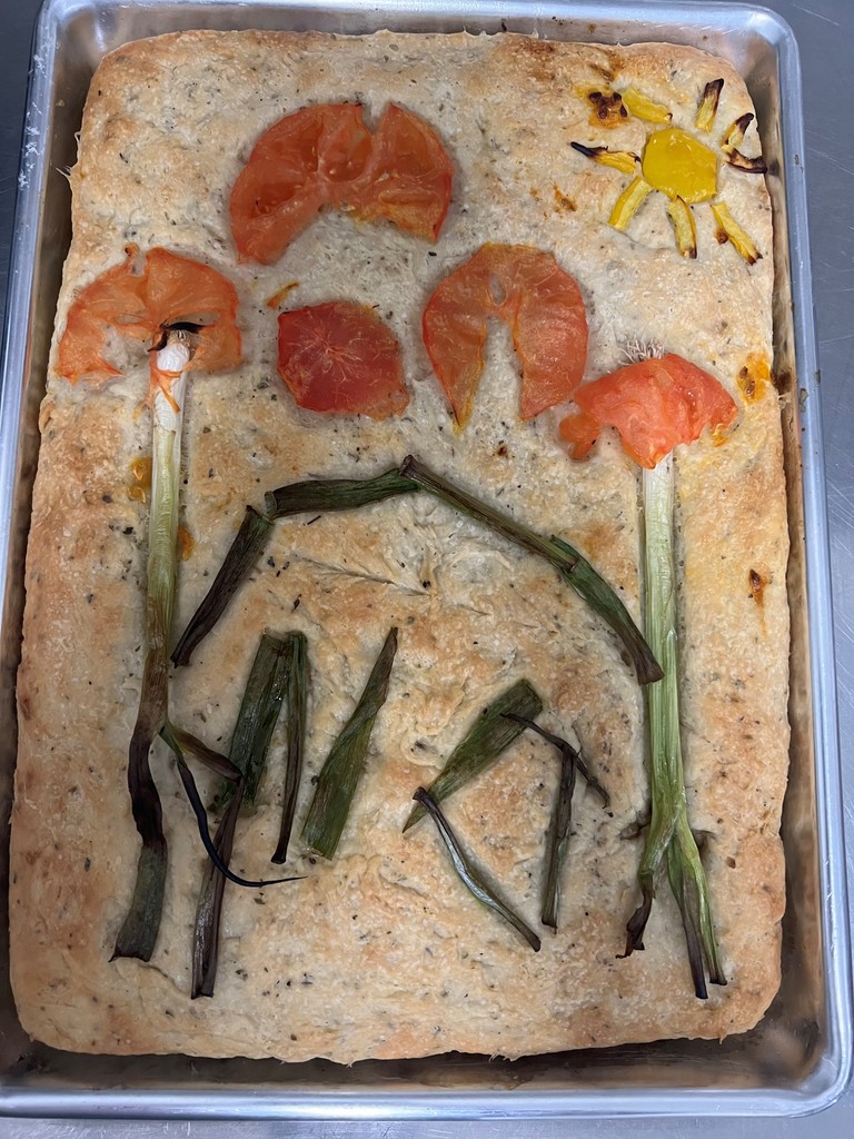 A gardenscape focaccia bread with flowers, a sun and a building.