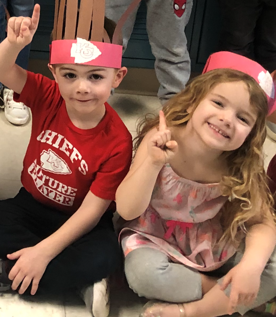 Two children with construction paper headbands raising their index finger to show that the Chiefs are number one.