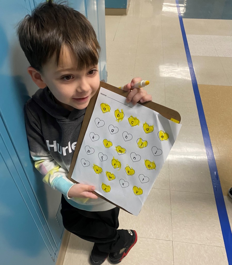 Child leaning on the lockers holding a clipboard with his letter hunt progress marked in yellow.