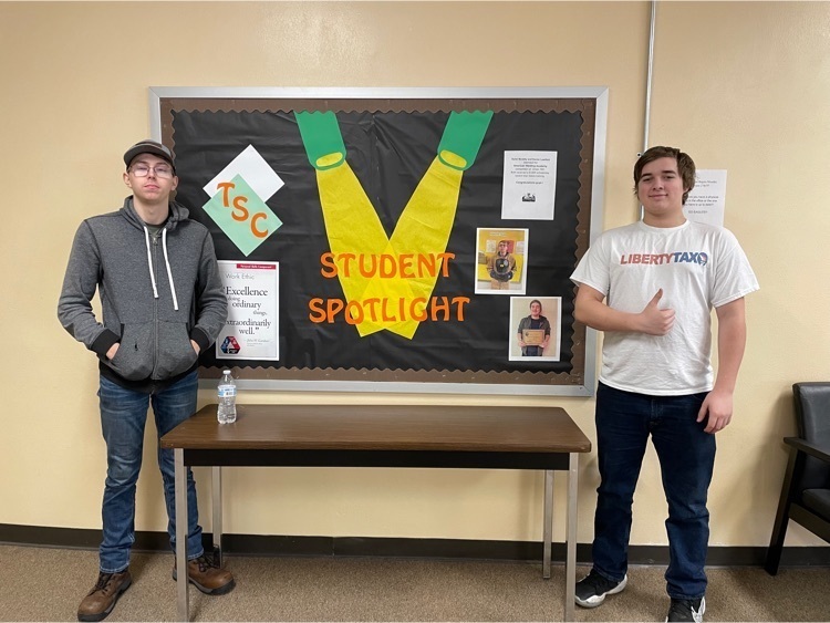 2 boys standing beside a “ TSC Spotlight” bulletin board.