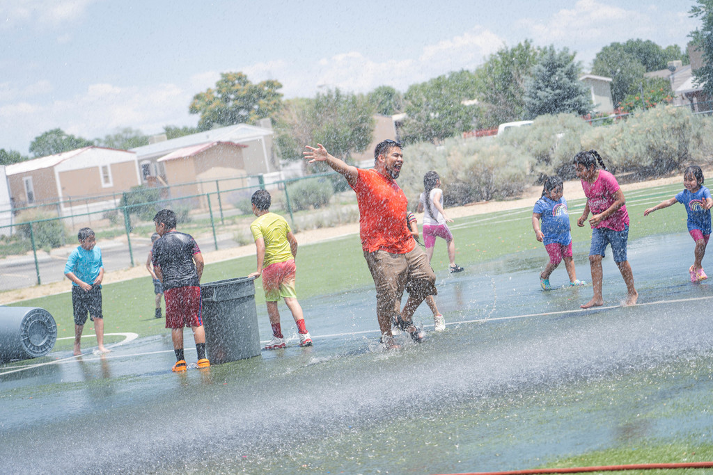 Teacher Bryan Cruz enjoying water from fire truck coming down over turf field with students