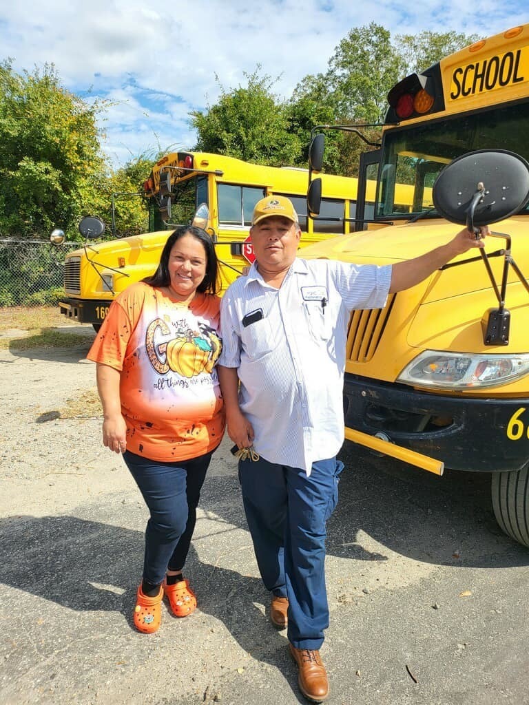 Woman and man smiling in front of school bus
