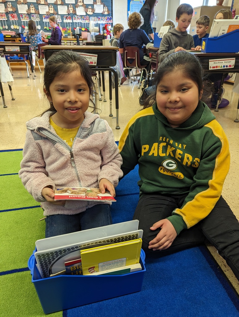 a 4th grade student reads a book with a 1st grade student on the floor