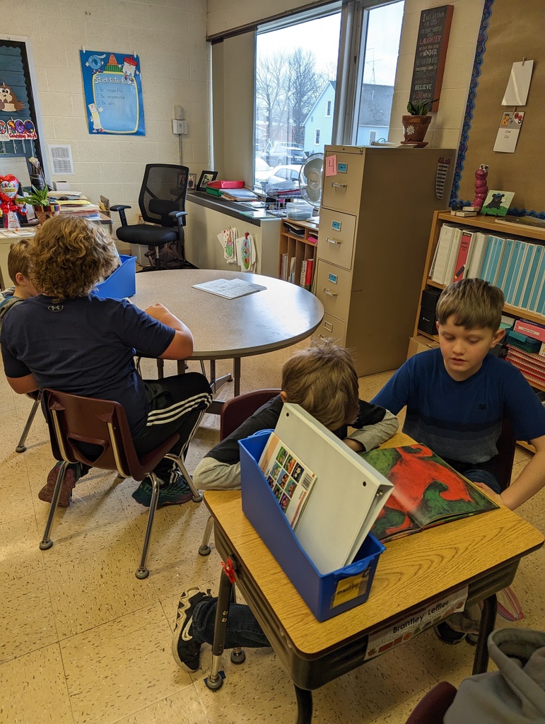 a 4th grade student reads a book with a 1st grade student on the floor
