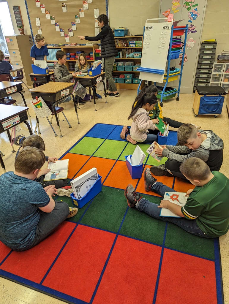 4th grade students sit with 1st grade students in their classrooms on the floor and read