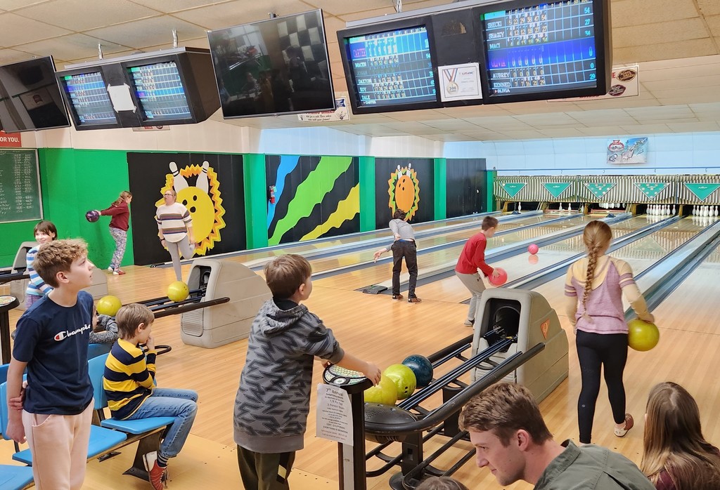2 students and a teacher are on the lane bowling while others look on