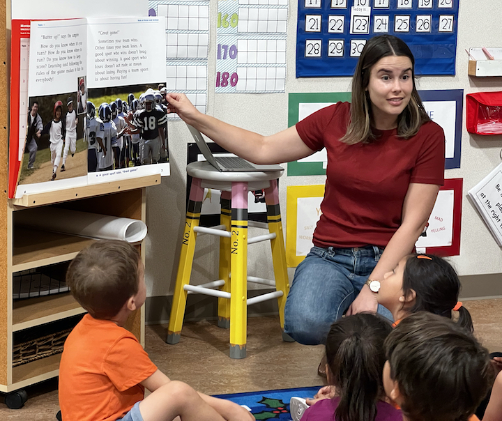 teacher kneeling reading large book