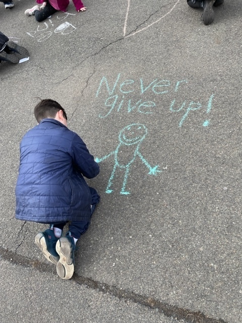 Wilson student drawing "never give up!" in chalkl