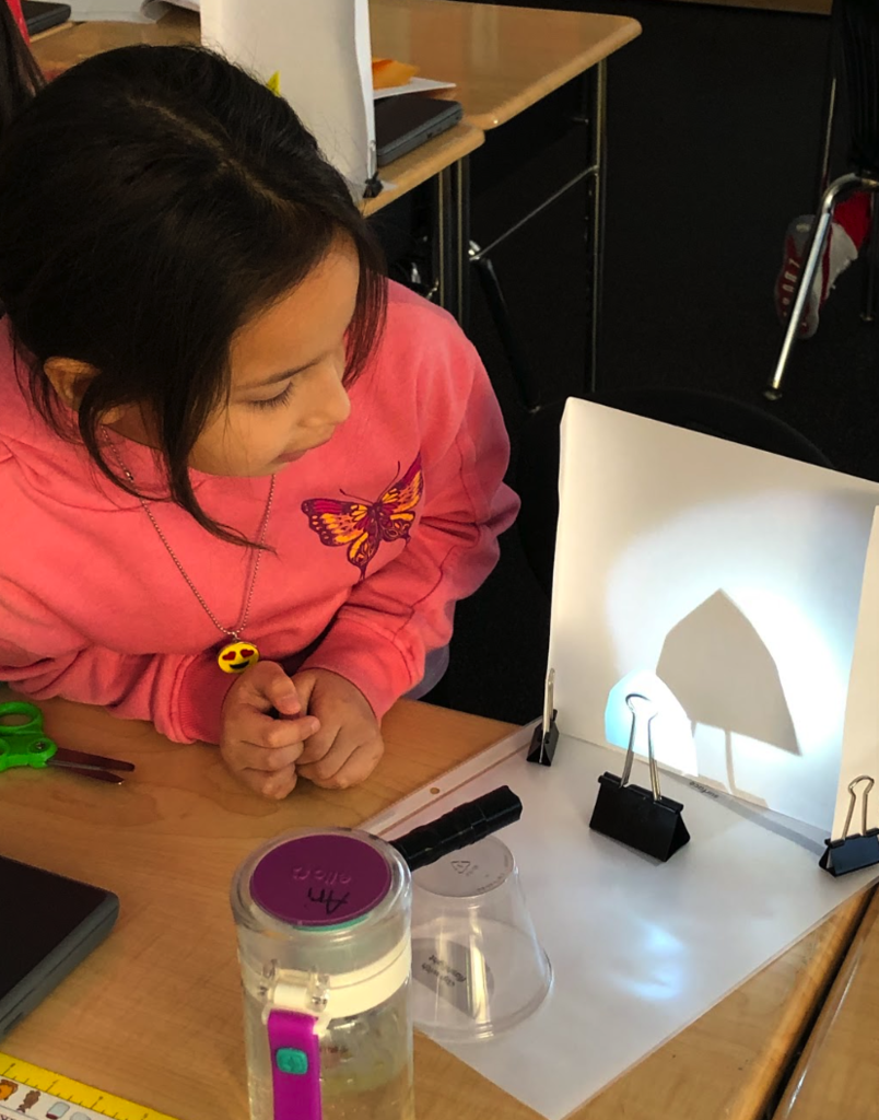 girl in pink top observes shadow that paper cutout makes against a backlit background