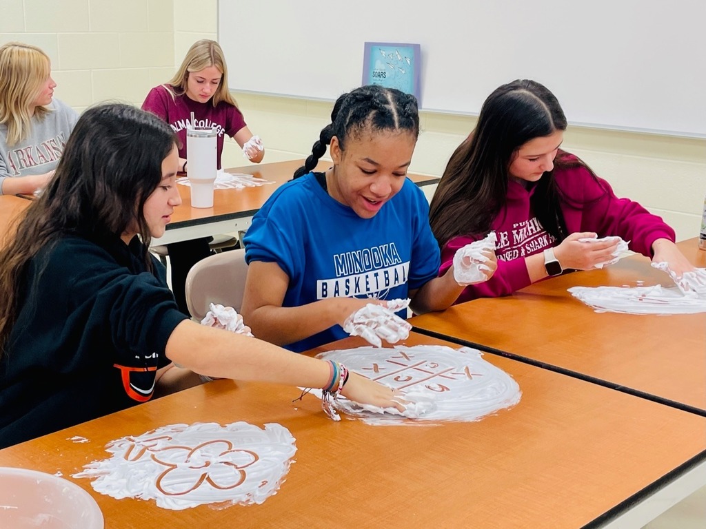 students with shaving cream smeared on the table with pictures traced out in them.  One is a flower.