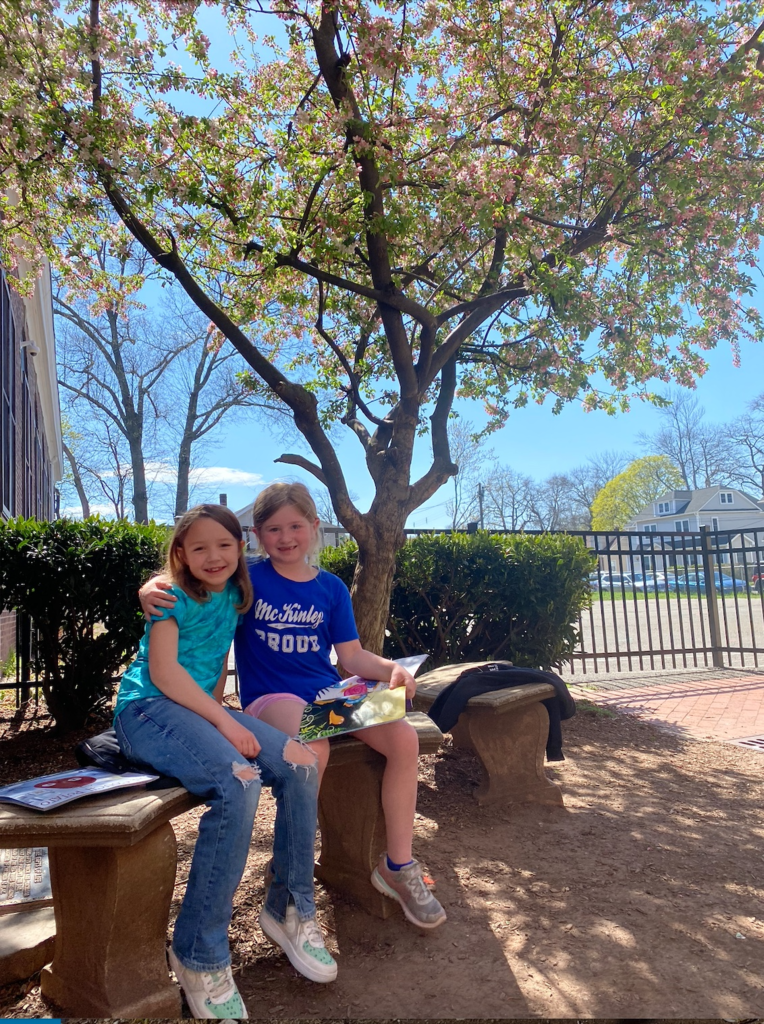 Two girls sit on a bench reading outside.