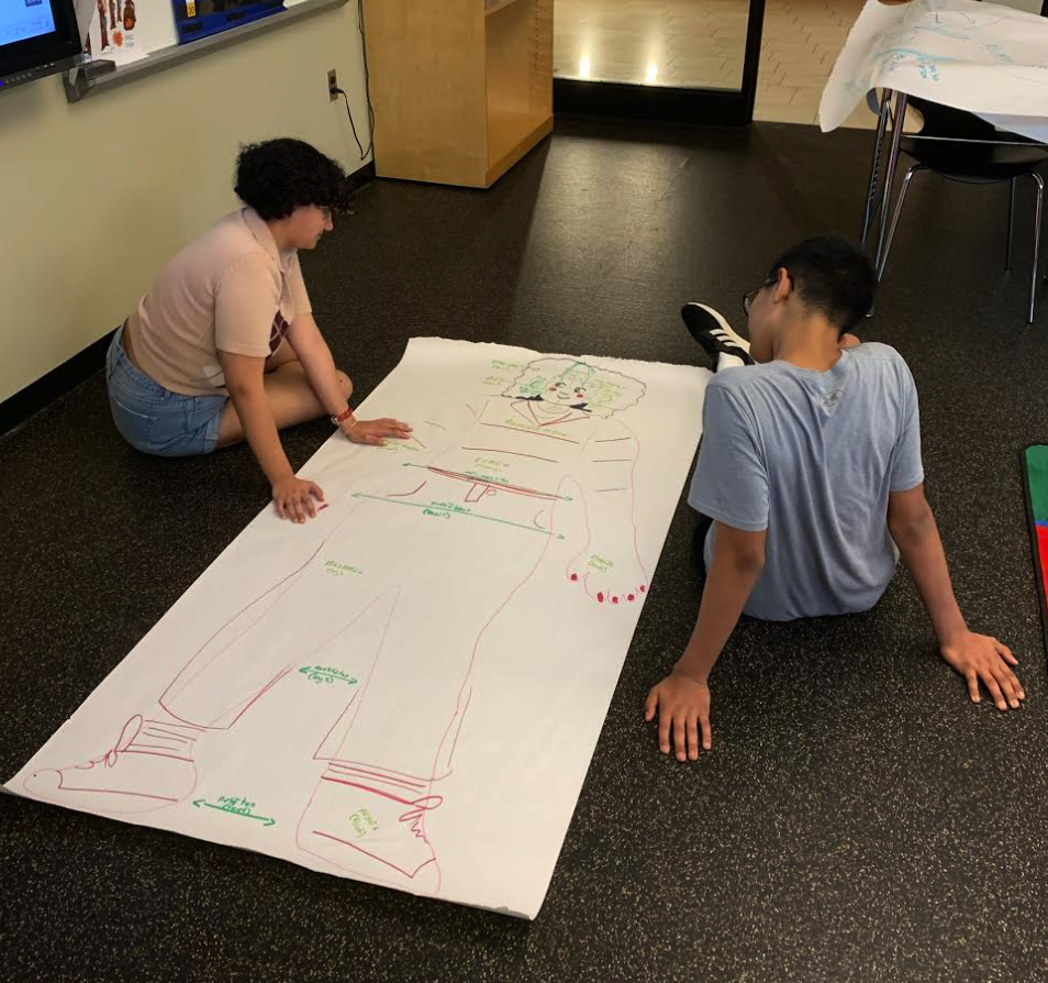 Two students on the floor looking at the tracing on paper and writing language words.