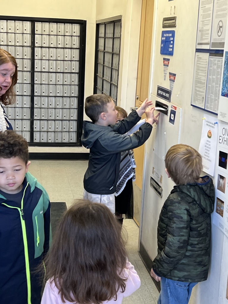 Students put a letter in a mail slot.