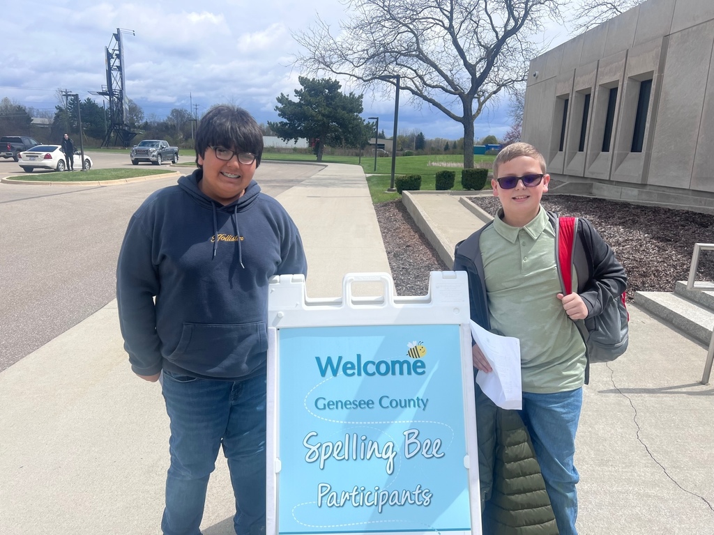 2 students standing by a sign for the spelling bee