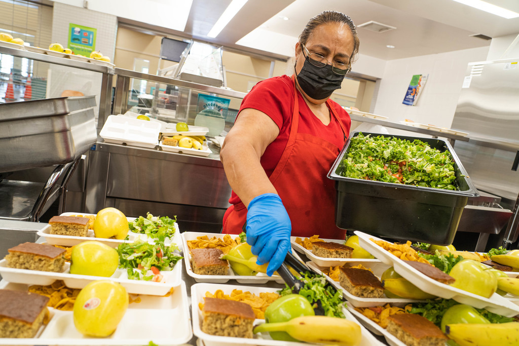Female student nutrition worker putting salad on a tray