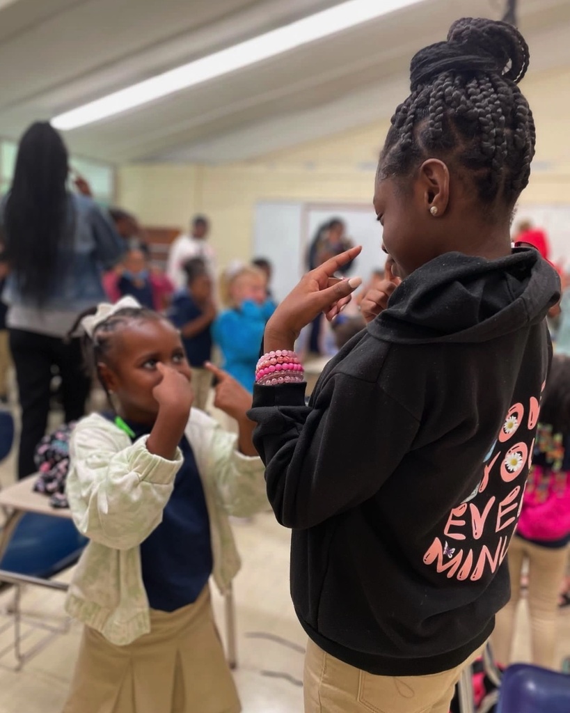 An older child and a younger child point to their eyes.