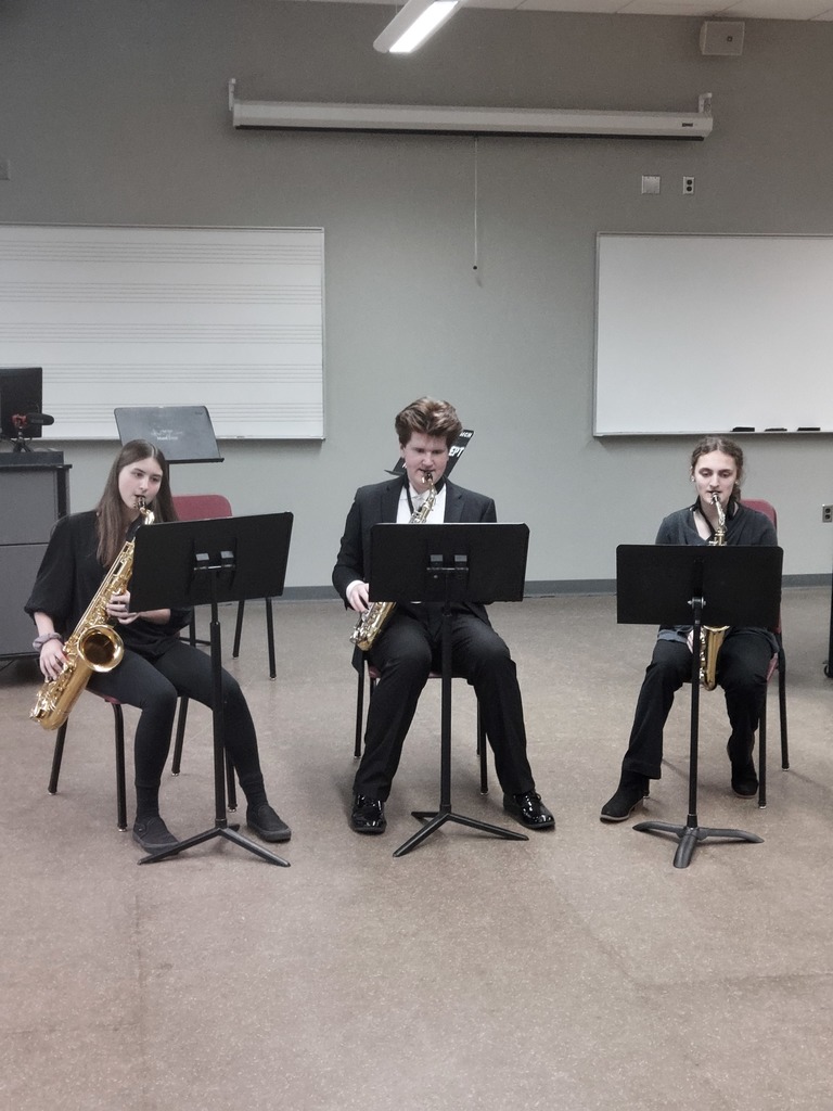 Three students sitting playing saxophones inside a classroom