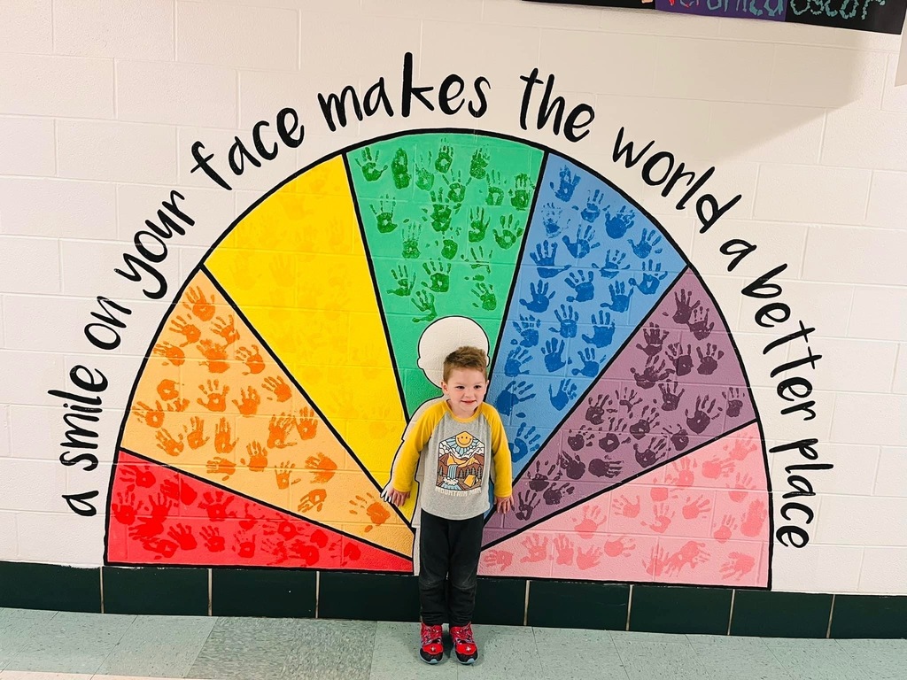 An incoming Kindergarten student poses in front of a mural