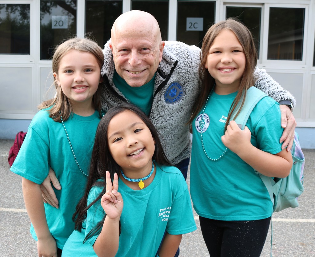 Principal poses for picture with three students, all wearing teal Food Allergy Awareness shirts