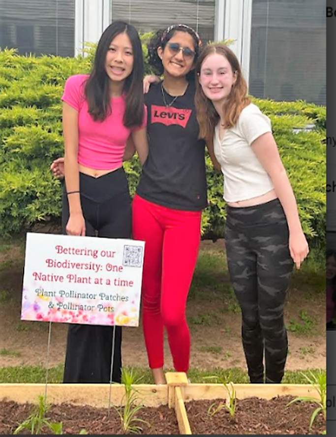 Three Edison students pose in front of newly planted pollinator garden