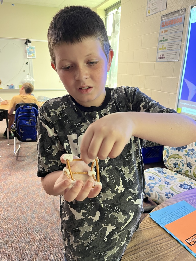 boy holding structure made of marshmallows and pretzel sticks