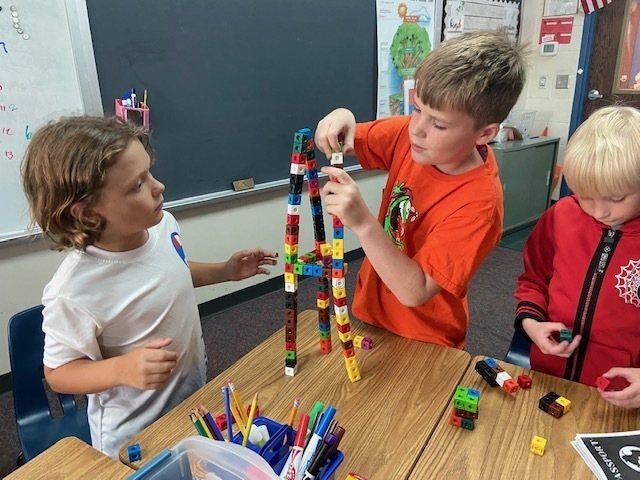 three boys building a structure out of cubes