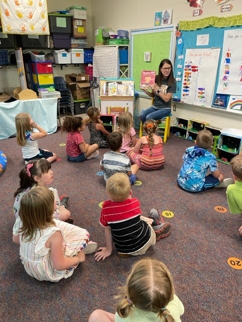 students sitting on the floor listening to a teacher read a book
