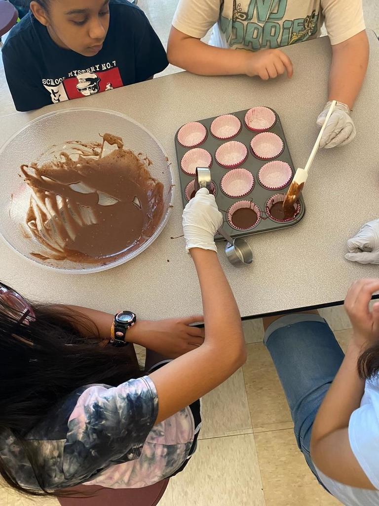 Students measure cake batter into cupcake tin