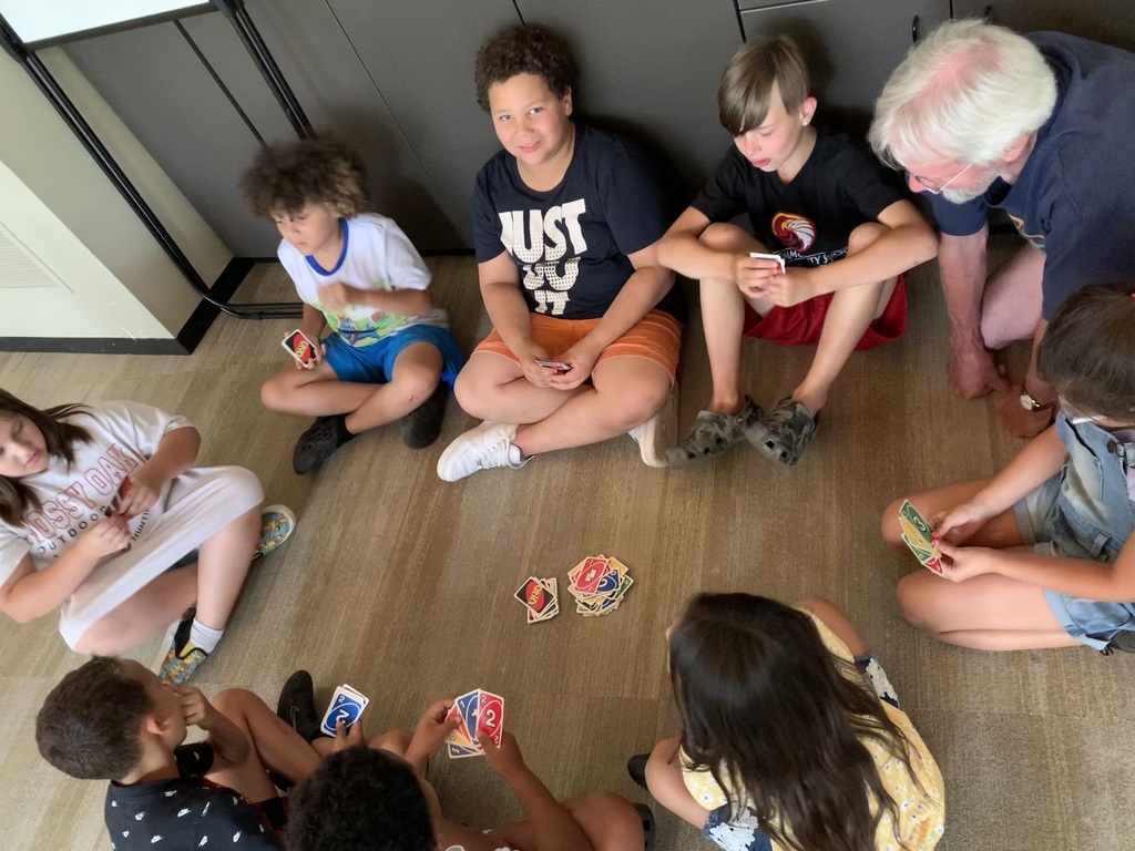 Students playing Uno, sitting on the floor inside their classroom.