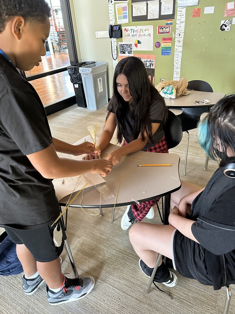Three students working with spaghetti noodles, tape and a marshmallow.