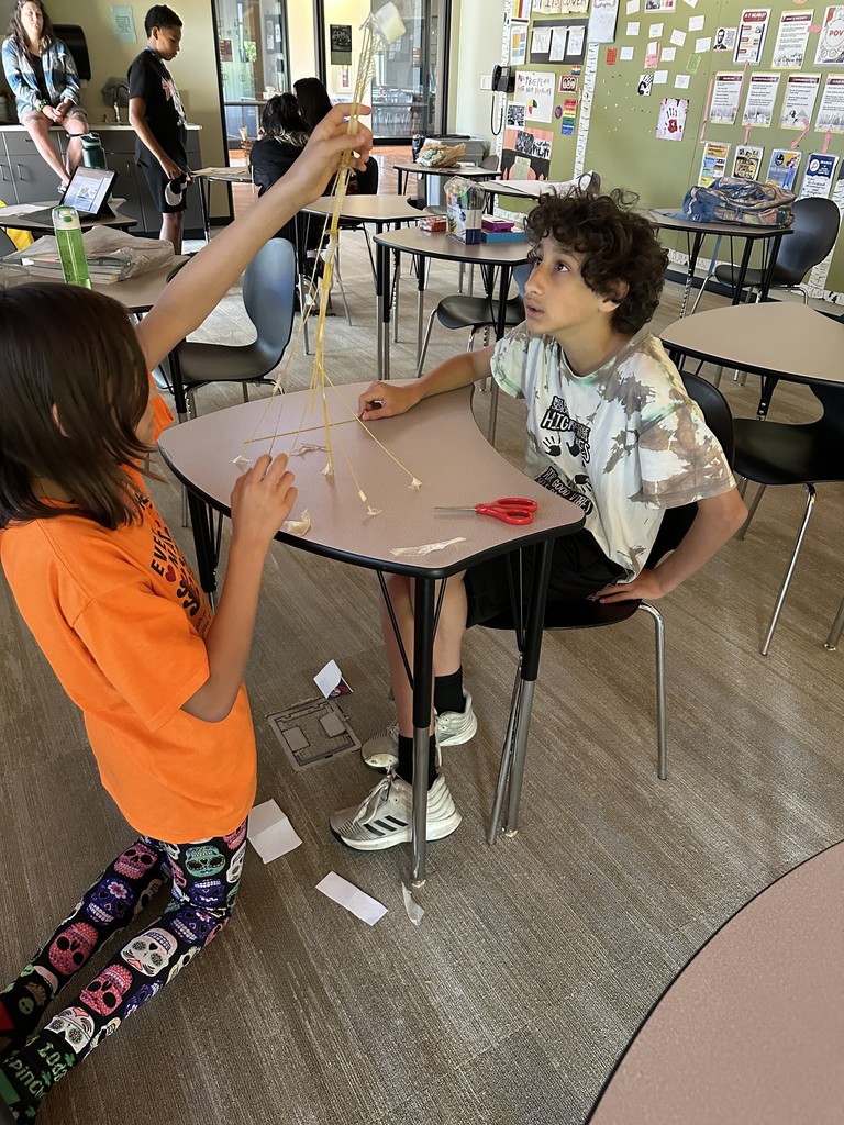 Two students working with spaghetti noodles, tape and a marshmallow.