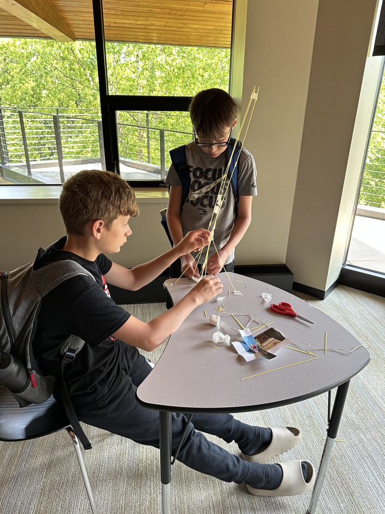 Two students working with spaghetti noodles, tape and a marshmallow.
