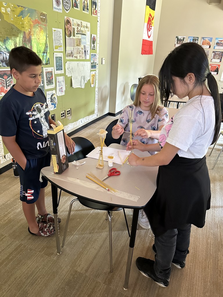 Three students working with spaghetti noodles, tape and a marshmallow.o