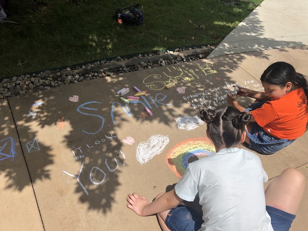 Two students writing messages using sidewalk chalk.