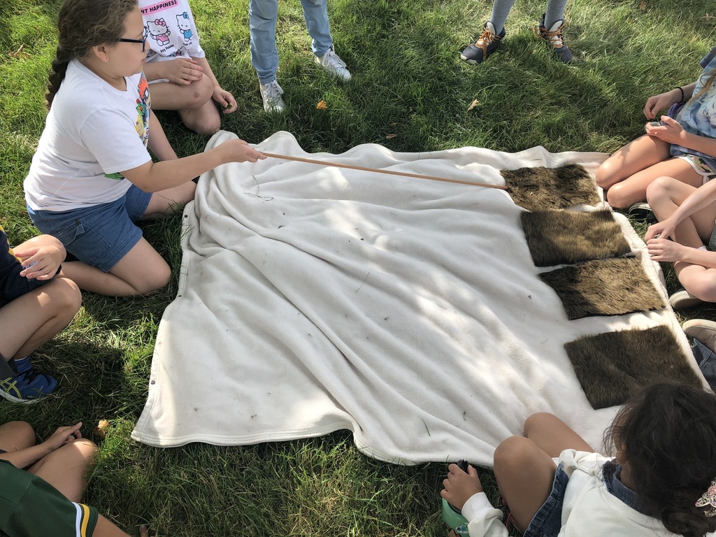 Girl pointing to furry squares on a blanket outside.