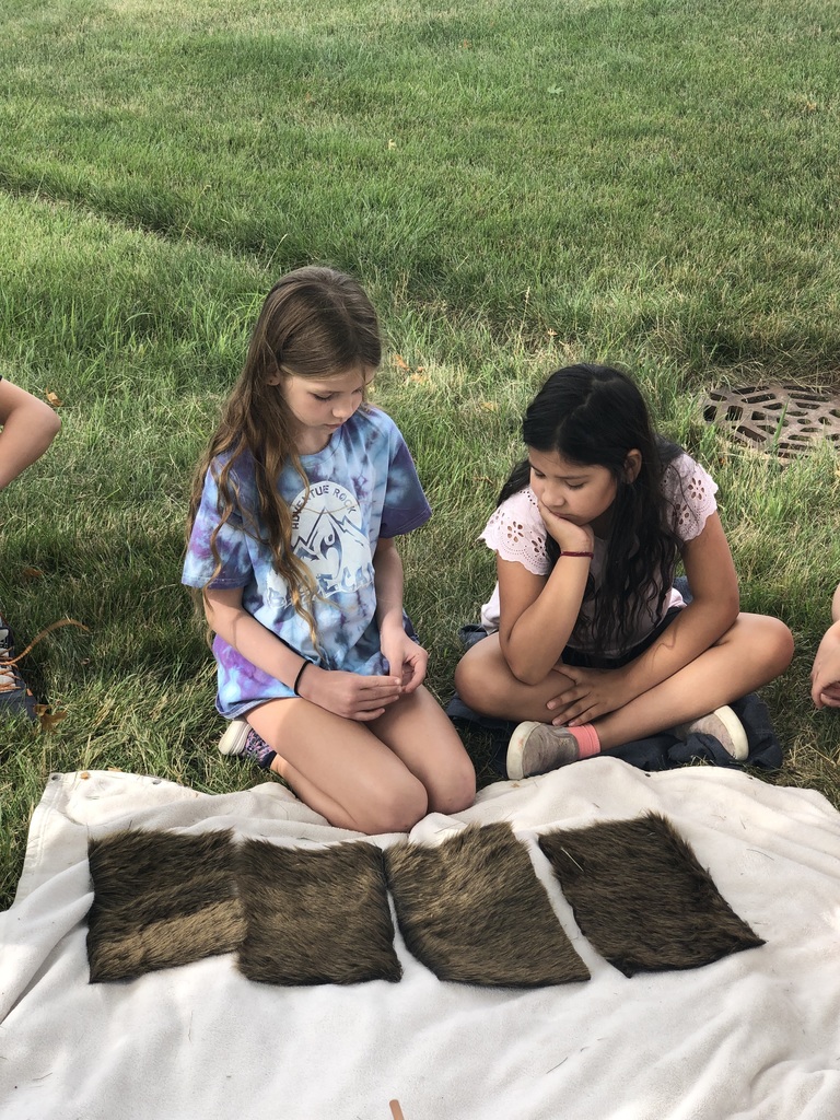 Two girls and furry squares on a blanket outside.