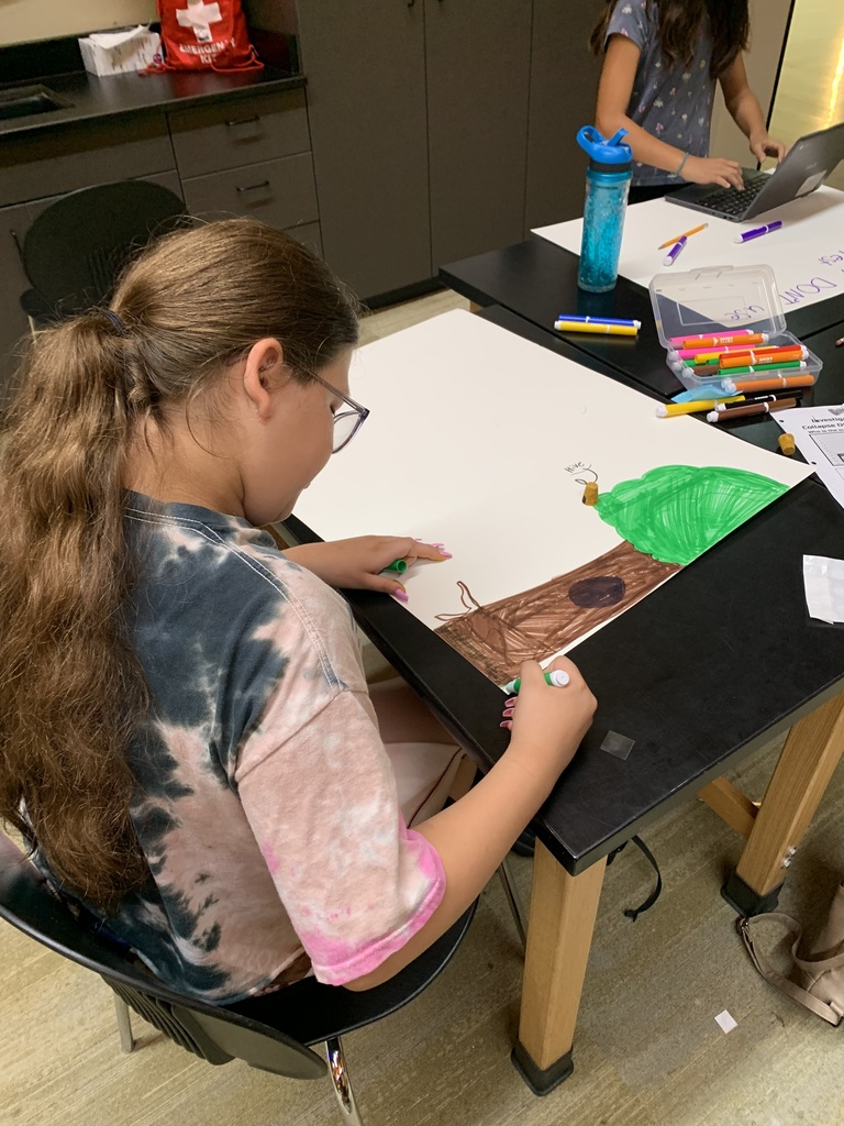 Student working on her hand drawn poster with a tree and beehive. 