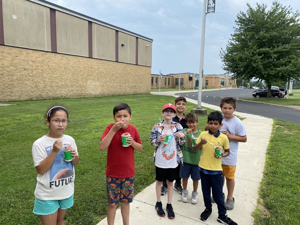 Students standing on the side walk outside the school eating Kona ice. 