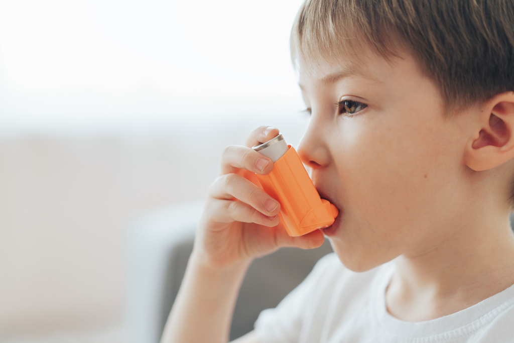 Little boy inhales medicine through an asthma inhaler