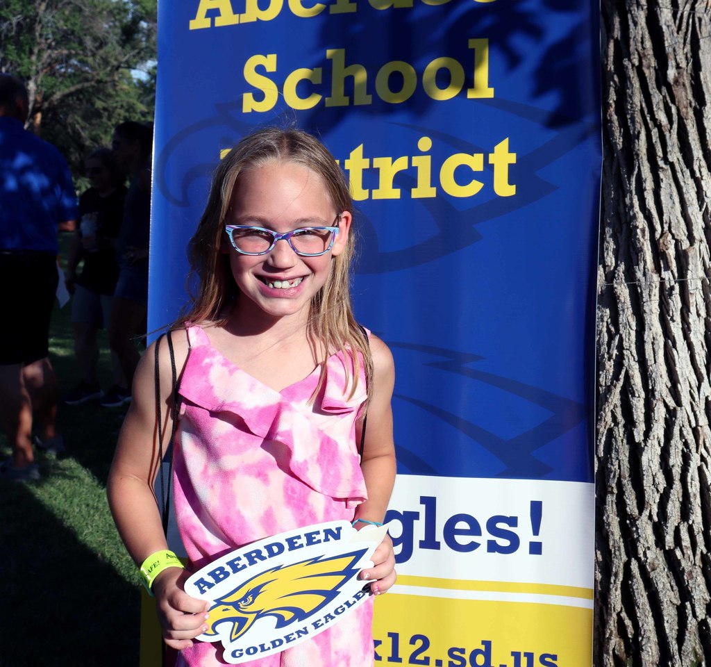 A student holding an Eagle sign in front of a school district backdrop at National Night Out