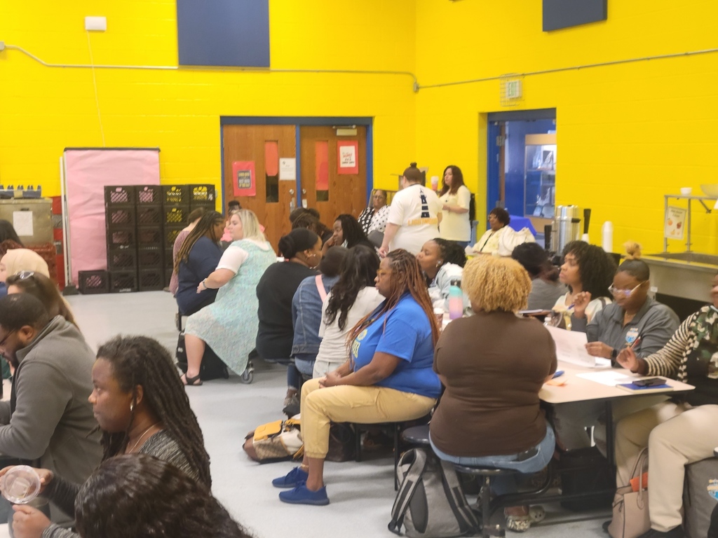 Many people sitting at cafeteria tables giveing attention to something not pictured